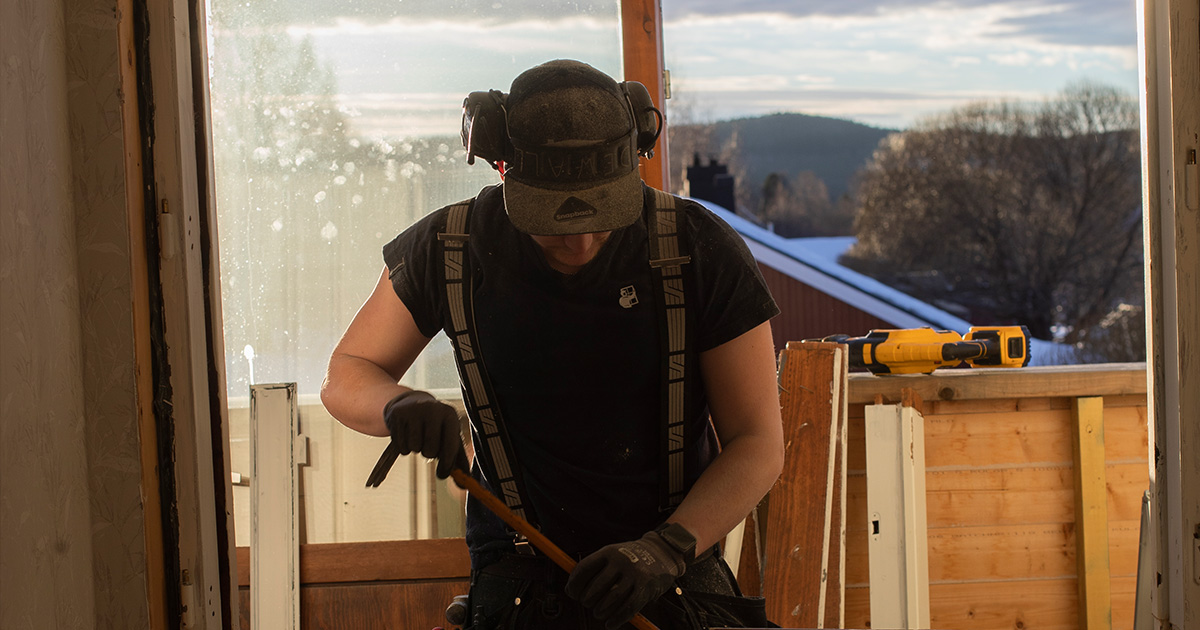 Hantverkare demonterar fönster inifrån ett hus i kvällsljus.