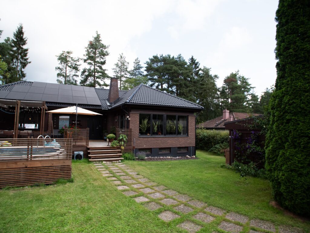 Brunt hus med altan, solpaneler på taket och trädgård med gräsmatta och gångstig.