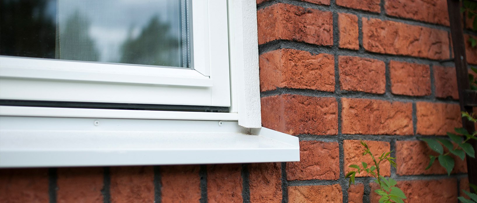 Närbild av fönsterbleck och vit fönsterkarm i röd tegelvägg.