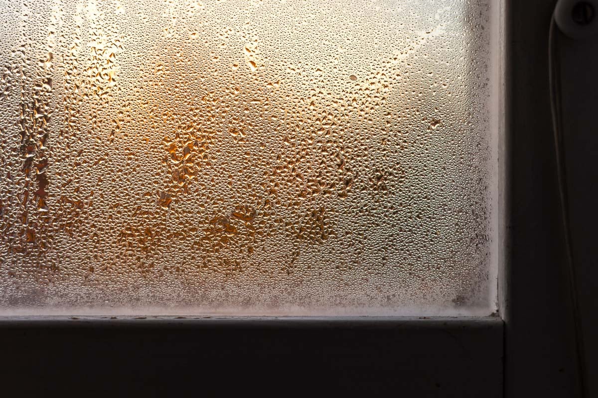 Kondens på fönsterglas i närbild med varmt ljus.