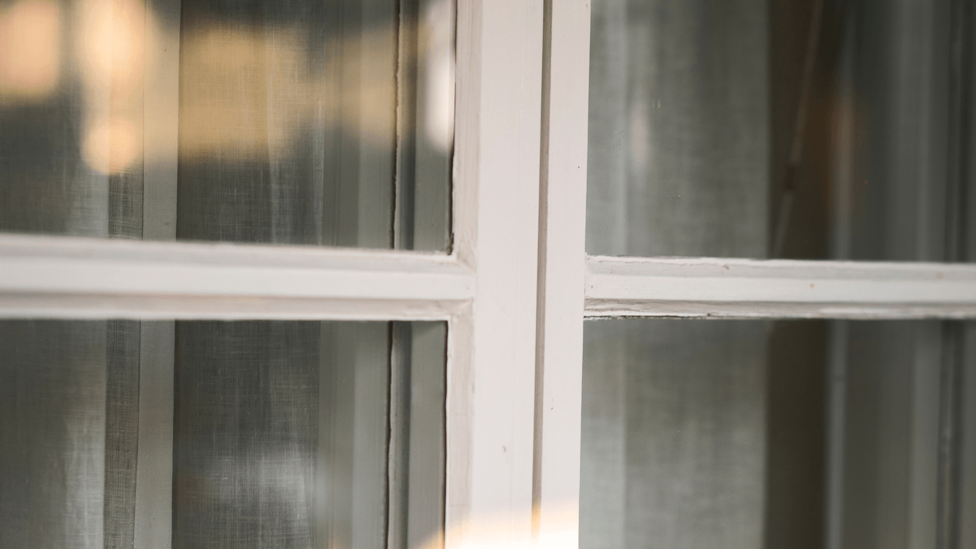Närbild av ett vitt spröjsat fönster med gardin bakom glaset.