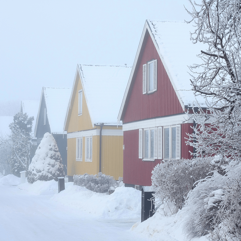 Färgglada trähus i rött, gult och svart i ett snötäckt vinterlandskap.