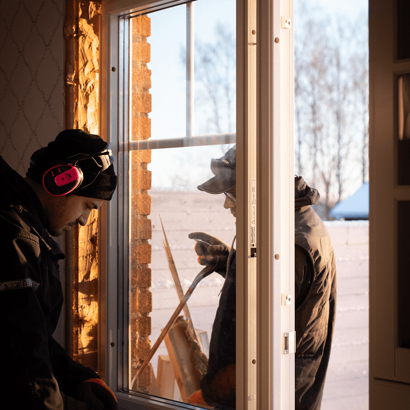 Hantverkare installerar ett fönster från insidan medan en kollega arbetar utanför.