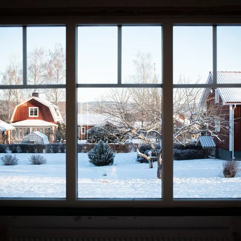 Utsikt genom ett stort fönster mot ett snötäckt kvarter med röda hus.
