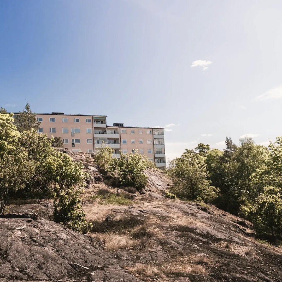 Flerbostadshus beläget på en klippa med natur och träd omkring.