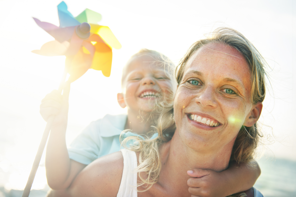 Förälder och barn leker utomhus i solljus med en färgglad leksak.