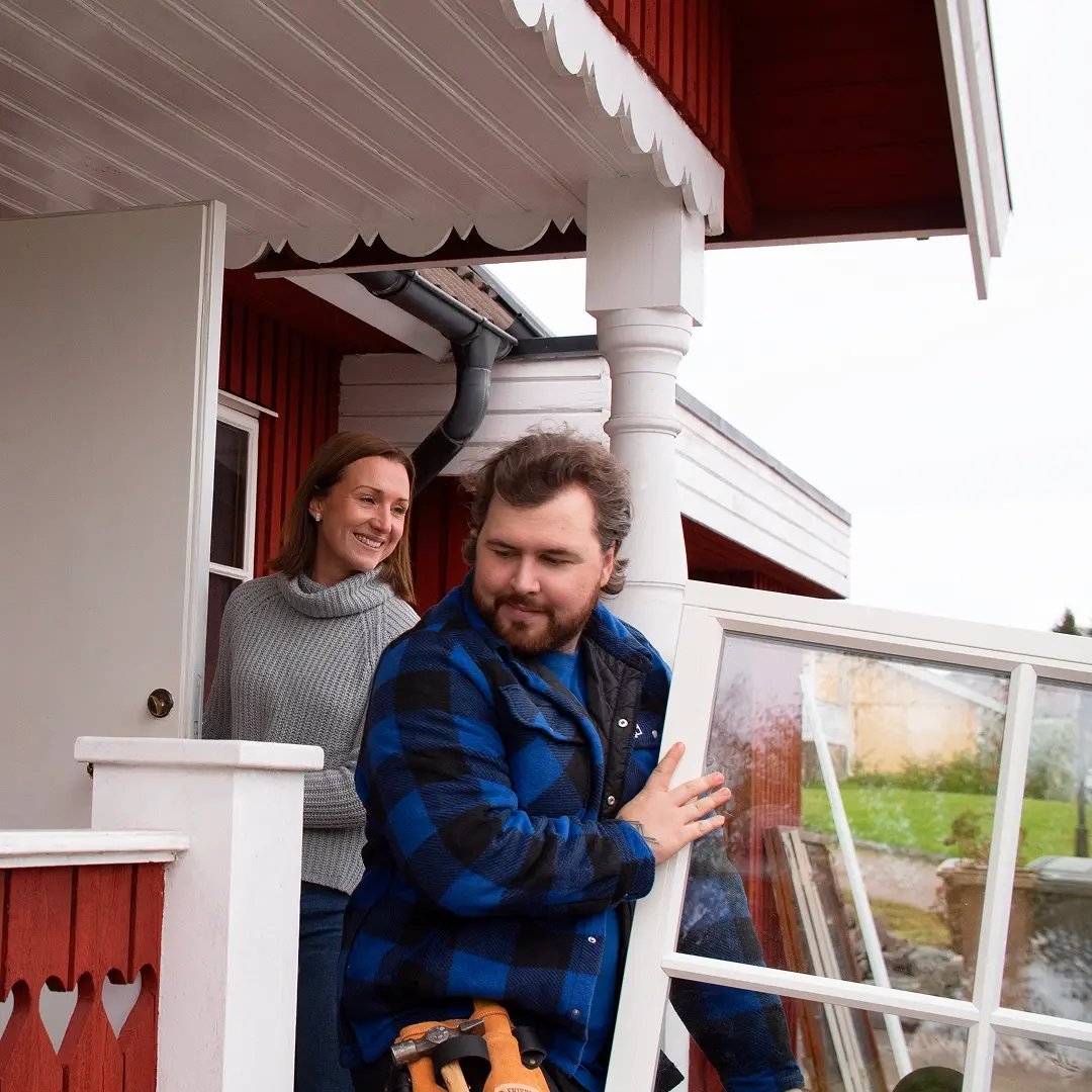 Person bär in ett fönster i ett hus medan en annan person står i dörröppningen.