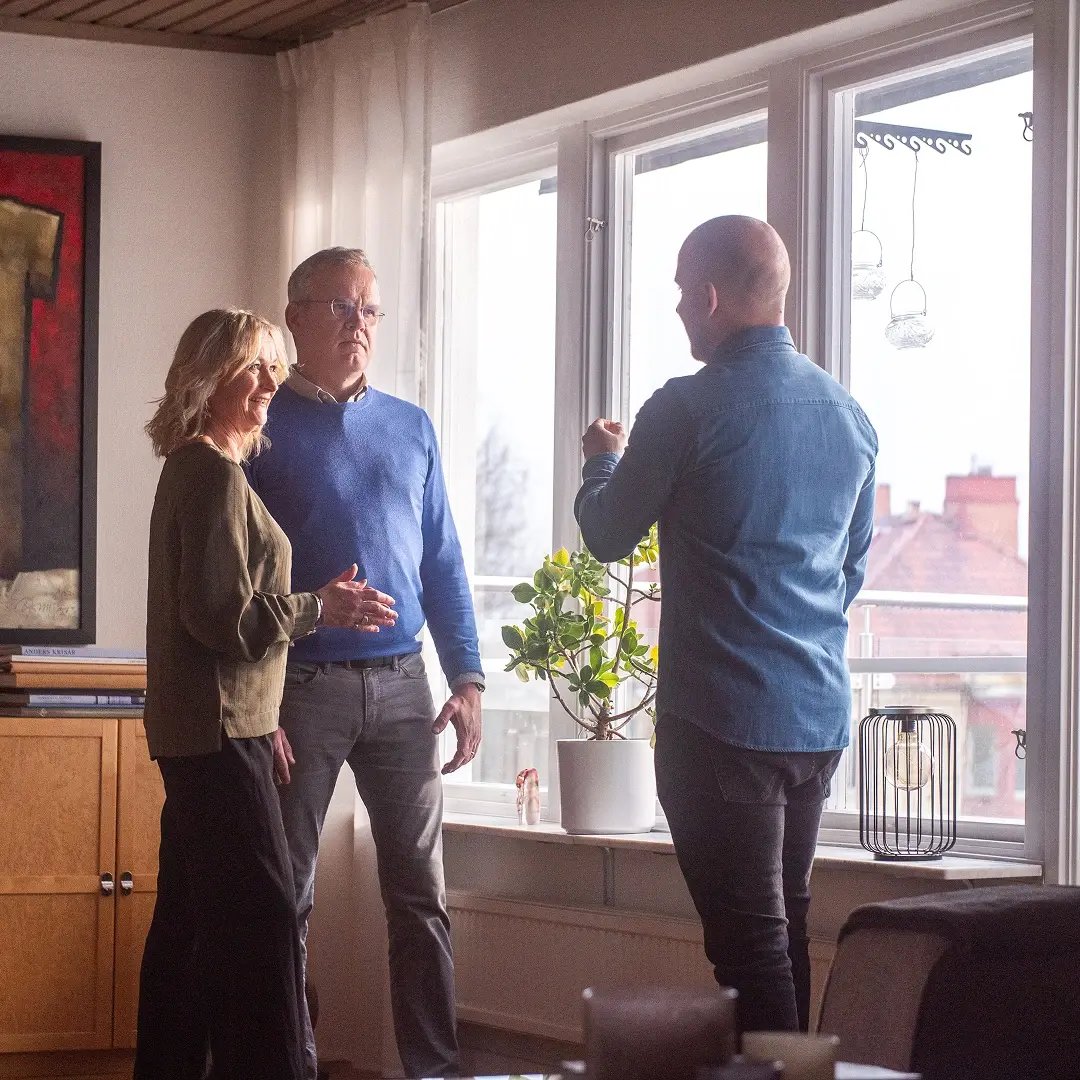 Rådgivare pratar med kundpar i vardagsrum framför stora fönster.