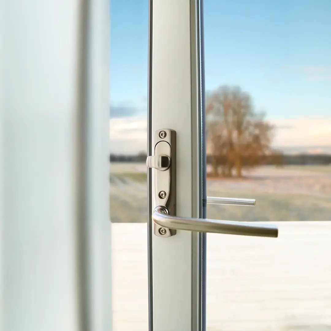 Närbild av ett dörrhandtag på en glasdörr med utsikt över ett landskap utanför.
