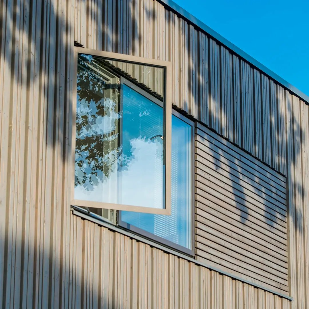 Öppet fönster på en modern träfasad med reflektion av träd och himmel i glaset.