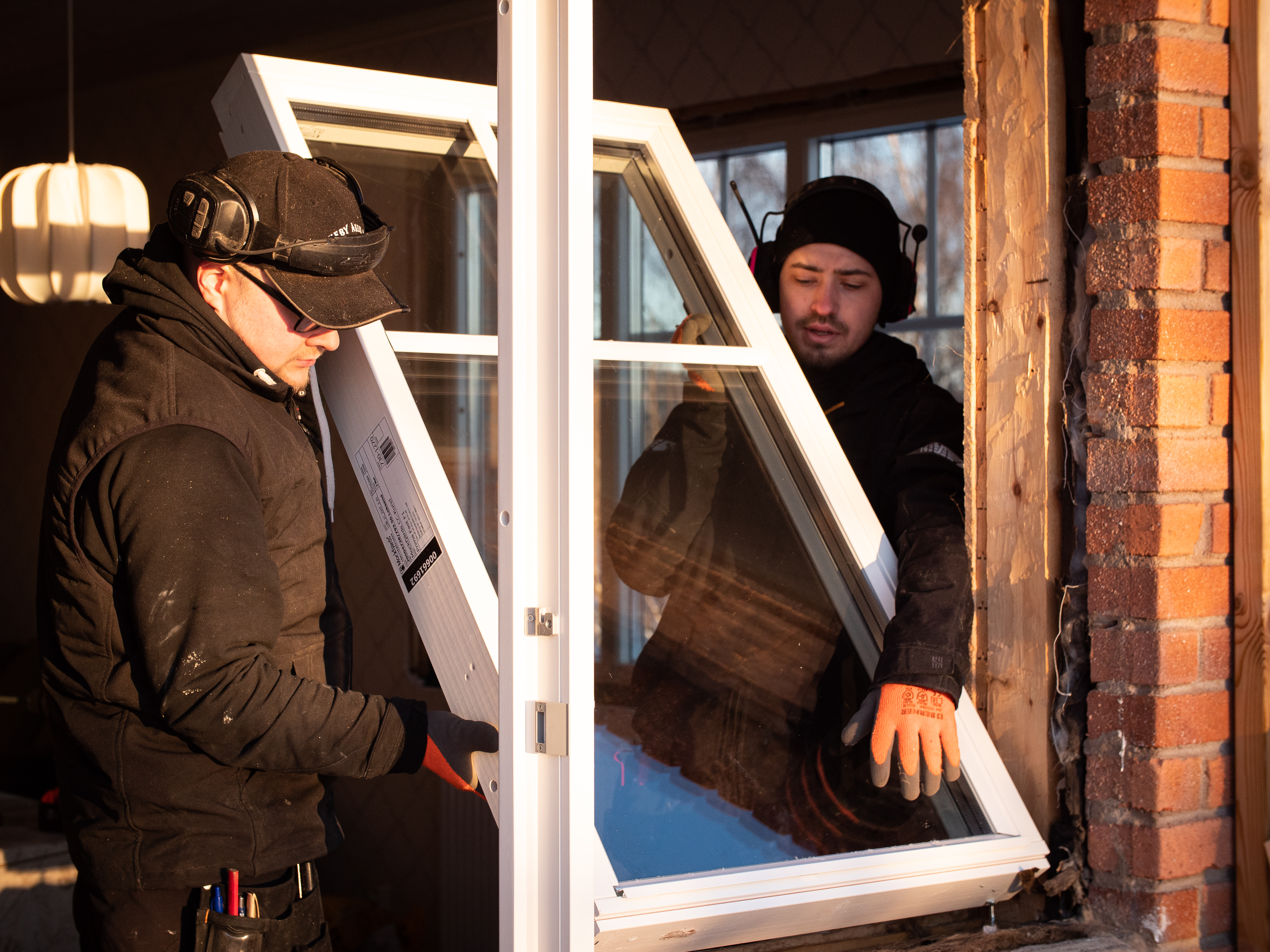 Två hantverkare installerar nytt fönster i husvägg.