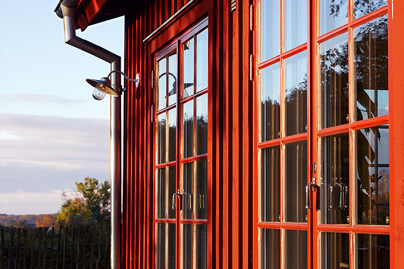 Röd träfasad med spröjsade fönster i kvällsljus.