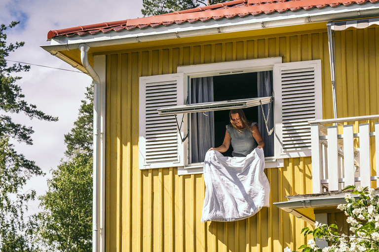 Kvinna vädrar genom öppet fönster i gul träfasad.