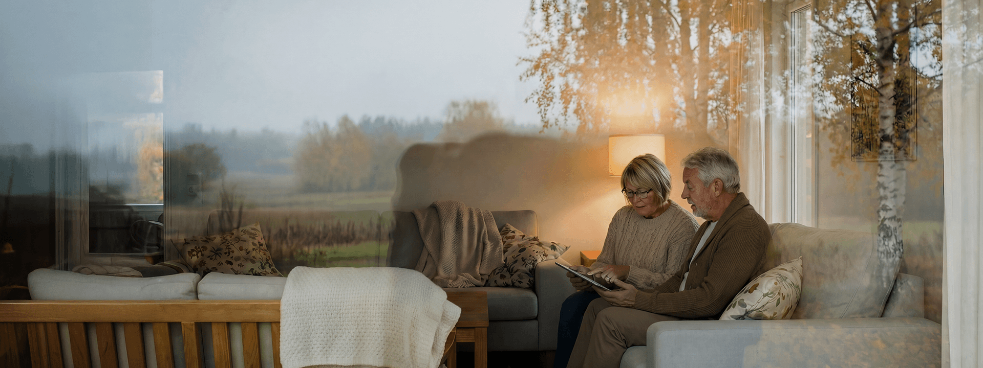 Äldre par sitter i en soffa vid ett stort fönster och tittar på en surfplatta.