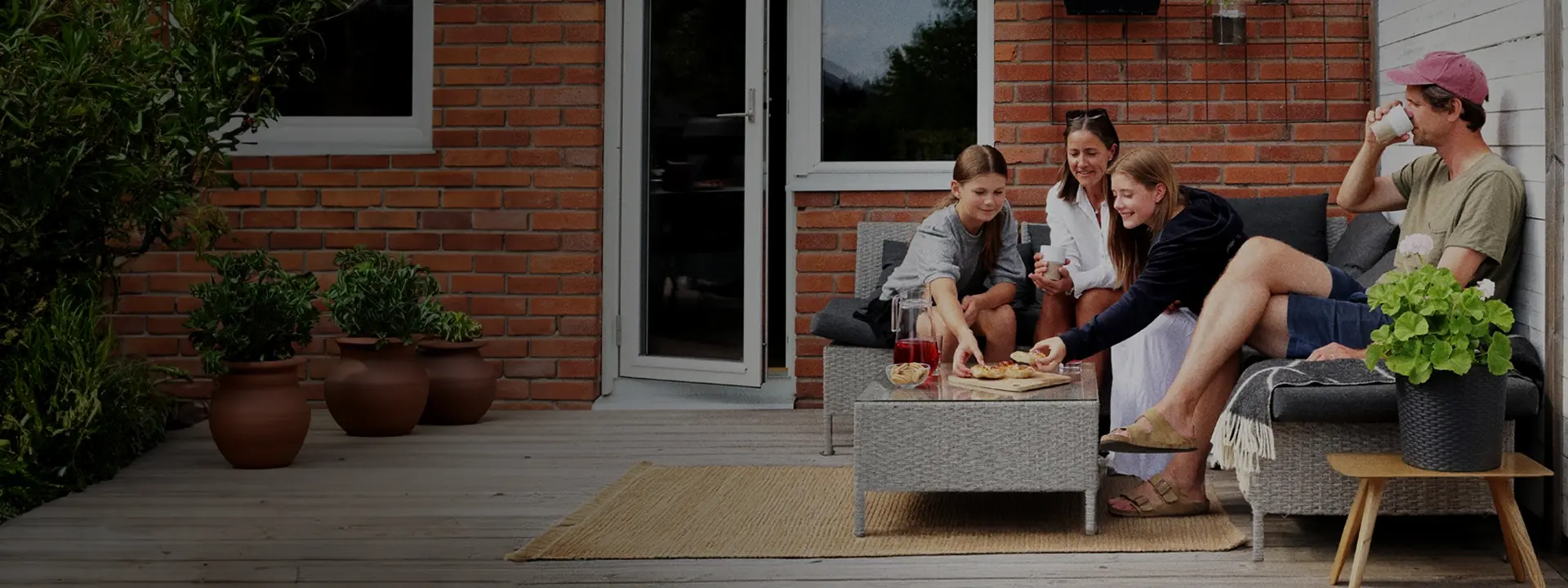 Familj sitter tillsammans på uteplats och fikar utanför hus.