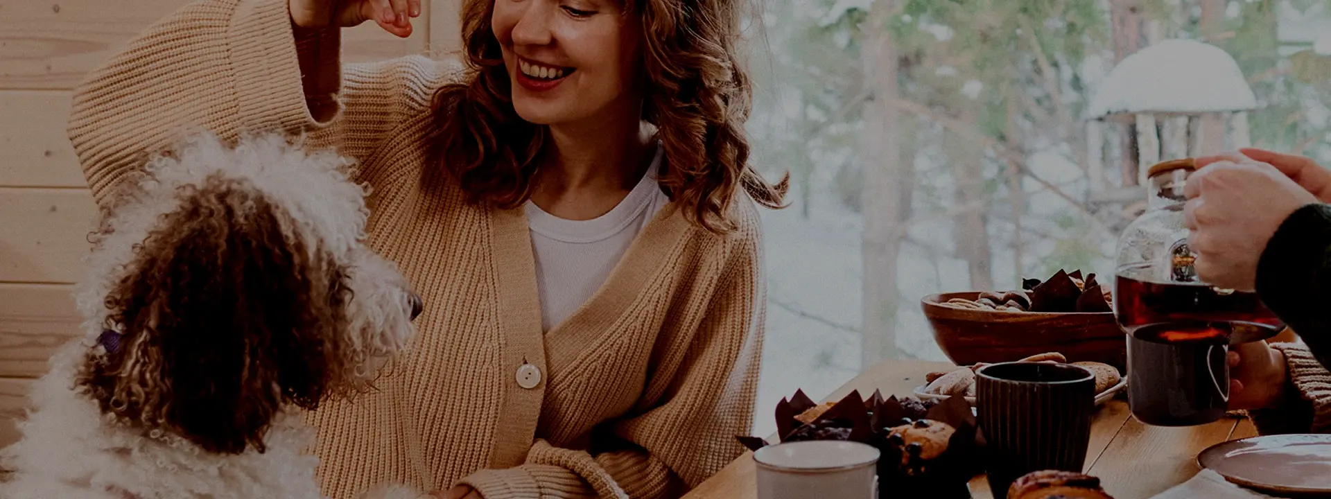 Kvinna sitter vid ett bord och leker med en liten hund, med fika framdukad.